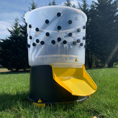 Hatching Time Cimuka. Large feather plucker can be seen sitting on grass to show scale size of plucker. Feather chute is visible and all-natural rubber plucker fingers can be seen through rust-proof food grade plastic tub.